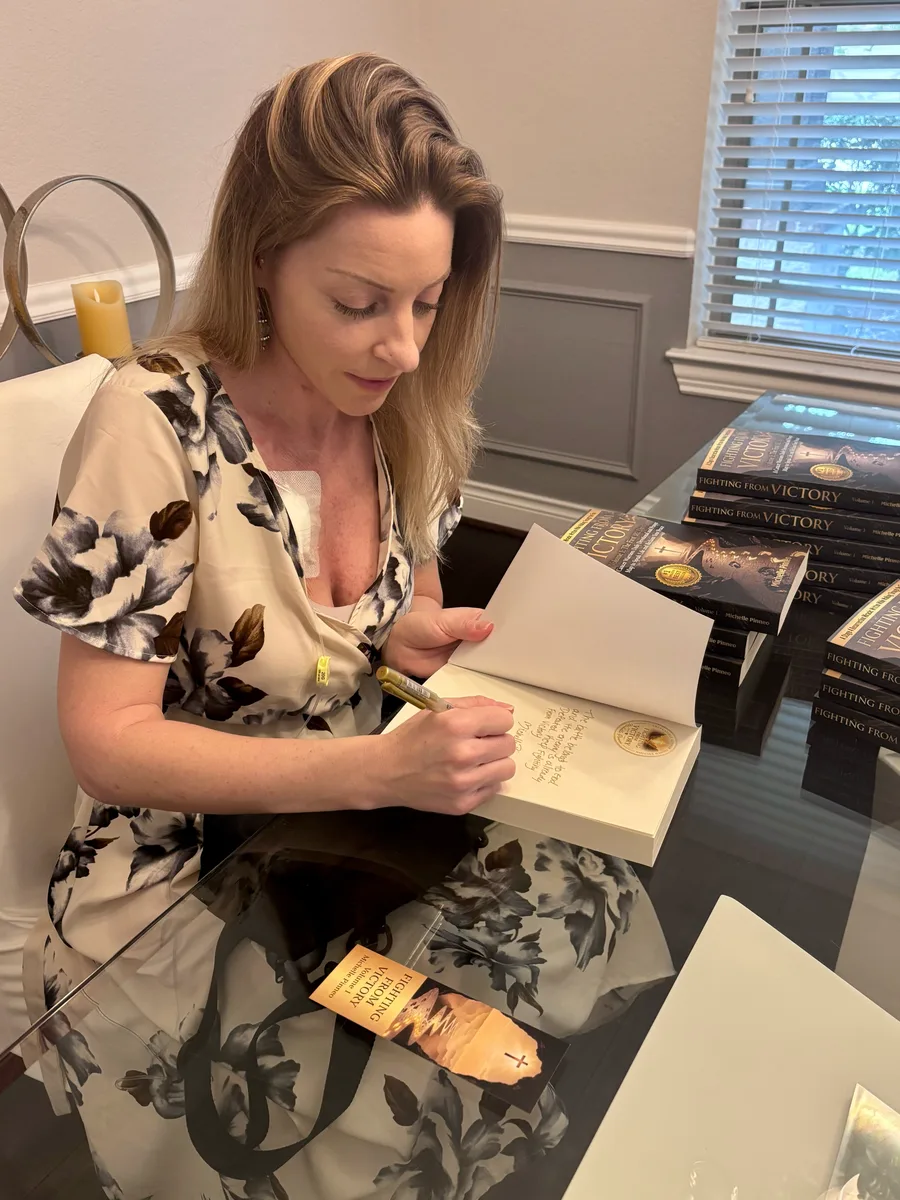 Michelle Pinneo signing copies of Fighting From Victory, with prayer bookmarks beside her